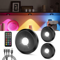 Black puck lights with remote control and cables on a white background, with colorful light display in the background.